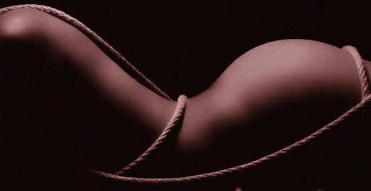 Shadowed nude body wrapped in textured rope against black background, artistic erotic silhouette