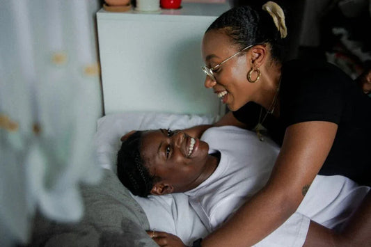 Smiling lesbian couple cuddling intimately on a bed in a cozy bedroom setting