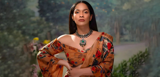 Confident woman wearing a vibrant printed saree and statement necklace in an outdoor garden setting