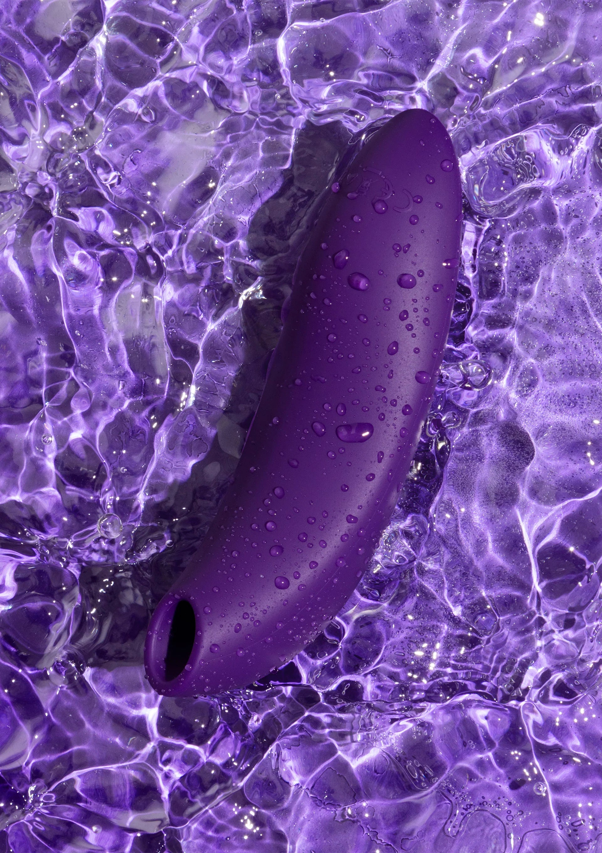 Donkerpaarse vibrator met knoppen, met druppels op het oppervlak in water