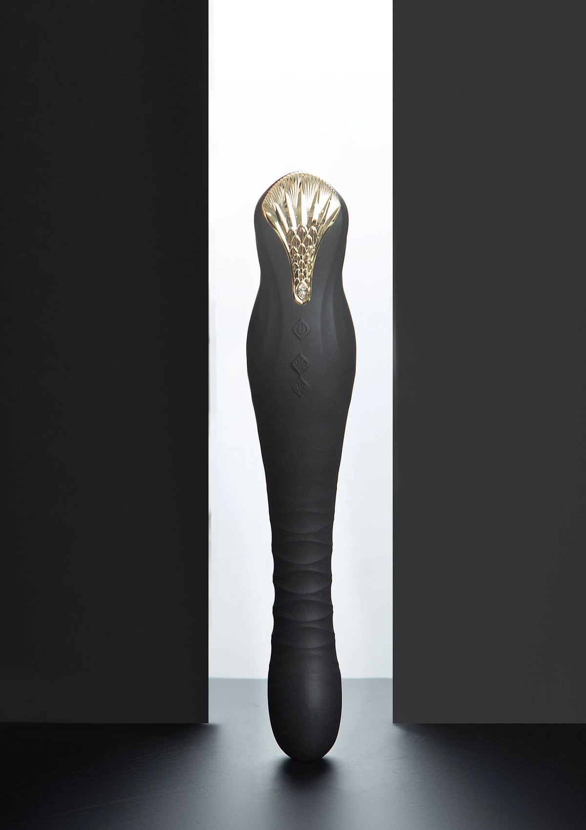 Zwarte dildo met goudkleurige kop en glanzende ribbels aan de bovenkant.